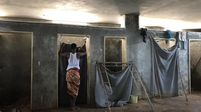 A detainee stands outside a toilet stall in the Ain Zara detention center, Tripoli, July 5, 2018. 