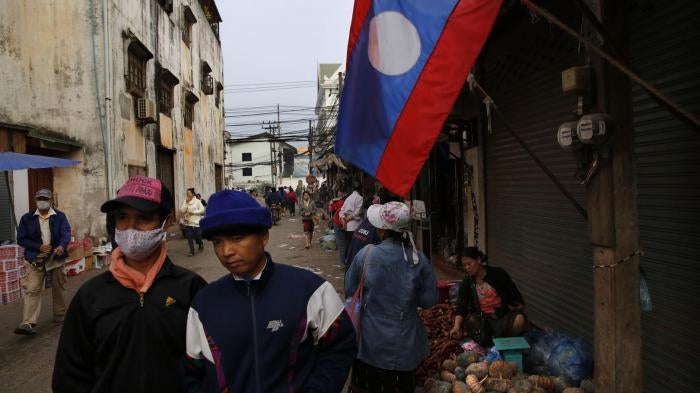 Lao people walk past their country flag, in the capital Vientiane, Laos. 