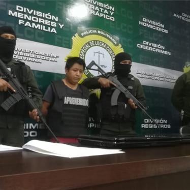 A man stands in front of a desk surrounded by armed soldiers