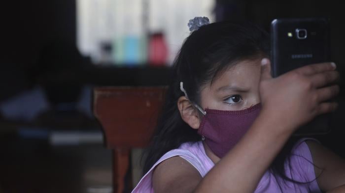 A young girl wearing a face mask holds up a cell phone