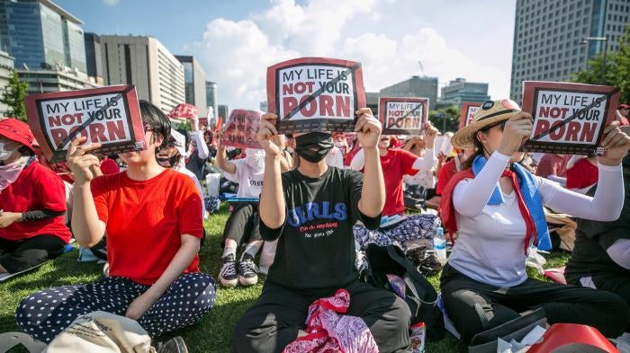 A group of women sit holding protest signs that read "My Life Is Not Your Porn"