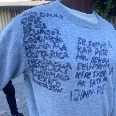 A Haitian who was returned to Haiti from the United States in December 2021 wrote on a sweatshirt the countries he had crossed to get to the US, starting in the Dominican Republic. The writing on the right says, in Creole, “This is the Lord who is rescuing us, he is the one who created heaven and earth.”