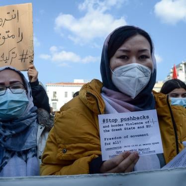 A woman at a protest holds a sign that reads "#StopPushbacks"