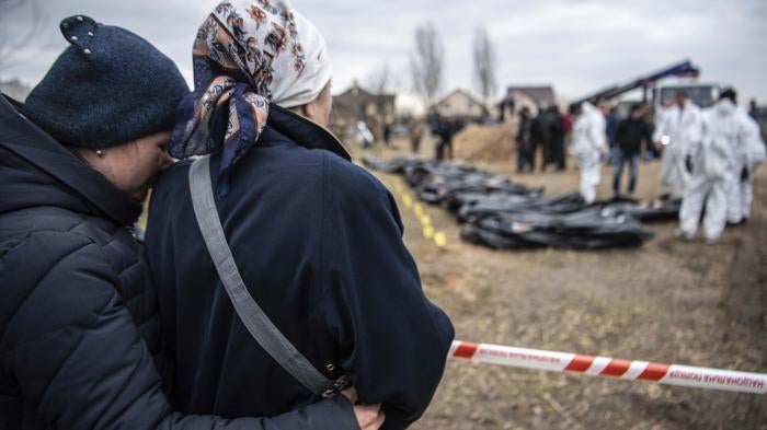 Women watch and embrace each other as bodies are exhumed from a mass grave by the authorities