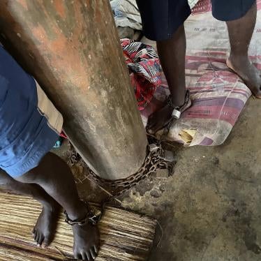 Two men are shown having one of their ankles chained to a log-like structure.