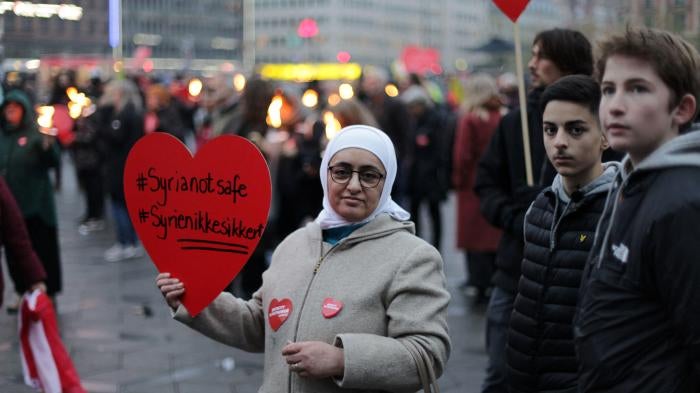 Syrian refugees hold a protest sign that reads "Syria Not Safe"