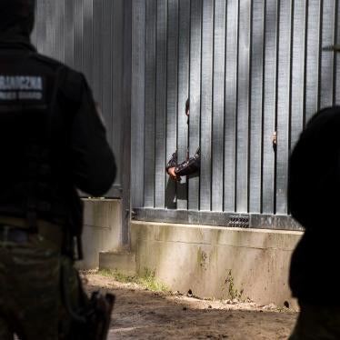 border guards watch asylum seekers stuck behind a border wall 