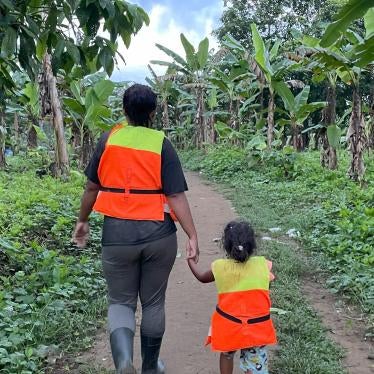 A Venezuelan woman, wearing a lifejacket, holds her daughter’s hand as they walk in a jungle