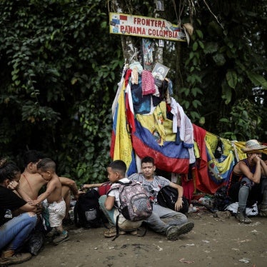 Migrants sit under a sign marking the Panama-Colombia border