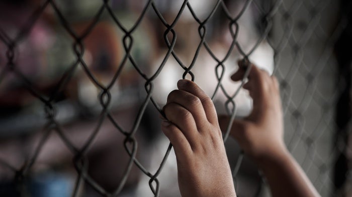  A young person holding onto a chain link fence.