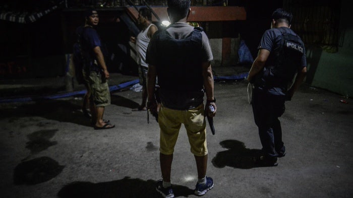 Policemen in plainclothes patrol a dark alley near the scene where three men were killed during a police anti-drug operation in Caloocan, Metro Manila, Philippines. 