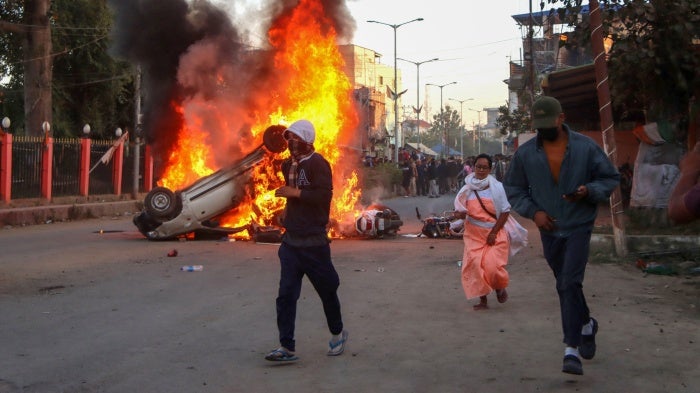 People run past burning vehicles of India's Bharatiya Janata Party (BJP) during a protest to condemn the alleged killing of women and children in Imphal, capital of India's northeastern state of Manipur, November 16, 2024.