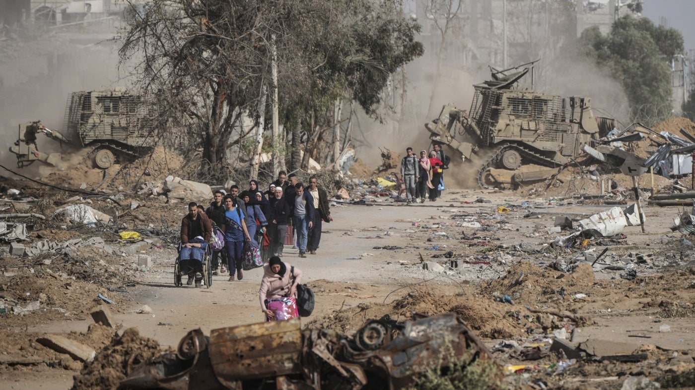 Families walk along a road with their possessions while smoke billows behind them