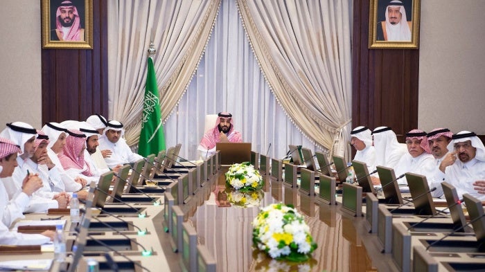 A man sits at the head of a large table during an official meeting,