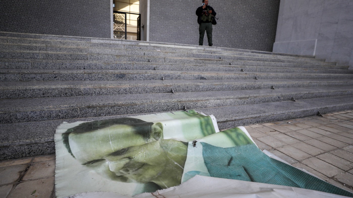 Une photo du président syrien Bashar al-Assad gît sur le sol tandis qu'un combattant de l'opposition syrienne se tient à proximité, à l'intérieur du palais présidentiel de Damas, en Syrie, le 8 décembre 2024.