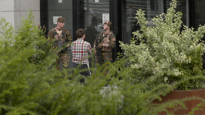 A photo of two Belgian soldiers speaking to a civilian.